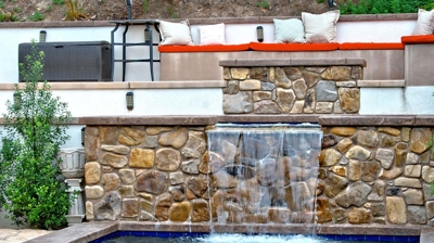 A wall made of rocks with a waterfall below a seating area Photo